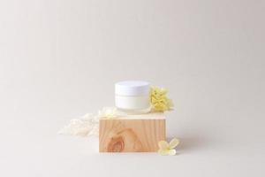 pot de crème cosmétique avec podium en bois et fleurs sur fond gris. gros plan, espace de copie photo