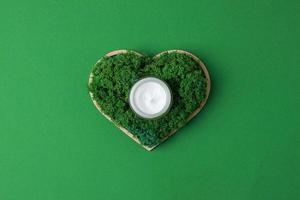 pot de crème cosmétique avec un coeur en bois et de la mousse sur fond vert. mise à plat, espace de copie photo