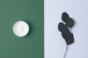 composition minimale avec pot de crème cosmétique et eucalyptus sur fond vert. mise à plat. photo