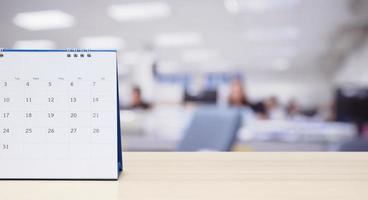 calendrier de bureau en papier blanc sur le dessus de table en bois avec fond intérieur de bureau flou photo