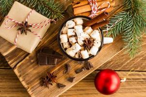 mug émaillé avec boisson au chocolat et guimauve sur une table de campagne en bois avec une boîte cadeau et des morceaux de chocolat à proximité. photo