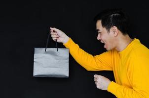 homme heureux asiatique tenant des sacs à provisions sur fond sombre pour le concept de vendredi noir. photo