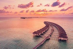 magnifique coucher de soleil paradisiaque des maldives. paysage aérien tropical, paysage marin, villas sur l'eau ciel de mer incroyable, plage de lagon, nature tropicale. destination touristique exotique, vacances aériennes d'été, vue sur drone. photo