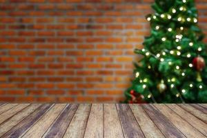 dessus de table en bois vide avec arbre de noël décoré flou avec des boules sur fond de mur de brique photo