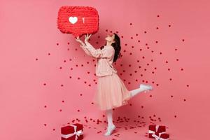 superbe fille dansant sur fond rose avec l'icône du cœur. photo de studio d'une femme célébrant la saint-valentin