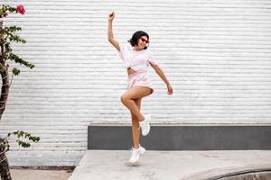 fille en baskets blanches sautant dans la rue. vue sur toute la longueur d'une femme dansante profitant de l'été. photo