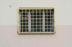 la texture du mur d'un immeuble résidentiel avec une fenêtre protégée par une grille métallique. ancienne méthode de protection du logement contre les voleurs photo