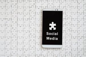 un grand smartphone moderne avec écran tactile se trouve sur un puzzle blanc dans un état assemblé avec inscription. des médias sociaux photo