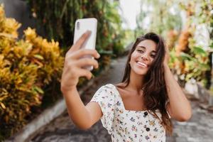 belle jeune femme en chemisier d'été blanc avec sourire pose pour selfie dans le jardin photo