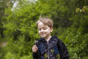 un garçon heureux un jour de printemps dans le jardin souffle sur des pissenlits blancs, des peluches s'envolent. le concept de loisirs de plein air dans l'enfance. portrait d'un garçon mignon. photo