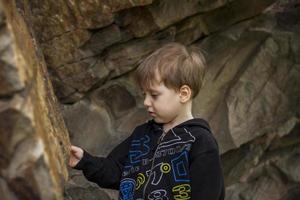 un garçon-enfant sur le fond d'une montagne rocheuse regarde quelque chose avec curiosité et est surpris. nature, rochers, montagnes. photo