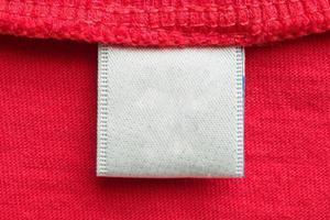 Étiquette de vêtements de soin de lessive blanche vierge sur fond de chemise en coton rouge photo