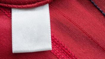 Étiquette de vêtements de soin de lessive blanche vierge sur fond de chemise de sport en polyester rouge photo