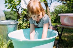 petite fille d'âge préscolaire aide à faire la lessive. enfant lave les vêtements dans le jardin photo