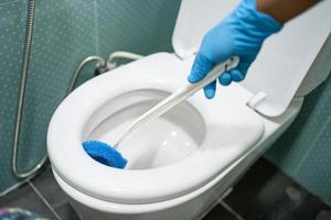femme de ménage nettoyant la cuvette des toilettes avec une brosse dans la salle de bain à la maison. photo