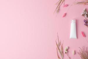 tube blanc de crème cosmétique avec des fleurs sur fond rose. mise à plat, espace de copie photo