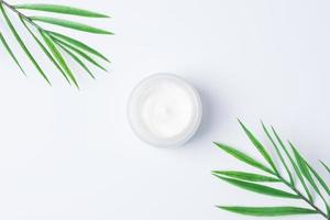 pot de crème cosmétique avec des feuilles de palmier sur fond blanc. mise à plat, espace de copie photo