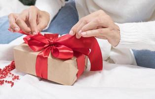 les mains féminines détachent un arc sur une boîte-cadeau pour noël dans un lit blanc. photo