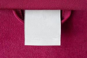 étiquette de vêtements de soin de lessive blanche vierge sur fond de texture de tissu rouge photo