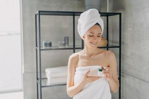 femme en serviette tient un pot avec des cosmétiques de soin de la peau dans la salle de bain. publicité cosmétique hydratante