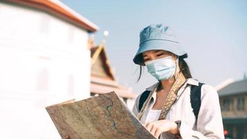 une femme asiatique voyageuse adulte porte un masque facial pour protéger le virus corona ou covid 19 en utilisant la carte pour rechercher la destination. photo