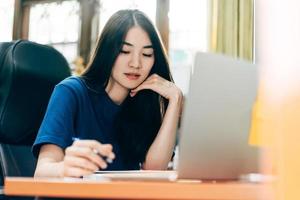jeune adulte indépendante femme asiatique utilisant un ordinateur portable et écrivant au bureau à domicile photo