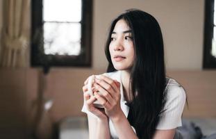 une jeune femme adulte asiatique tient une tasse de café le matin dans la chambre à la maison. photo