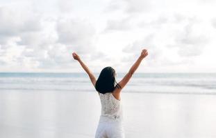 vue arrière d'une jeune femme asiatique adulte étirant la main et le bras ouvert se détendre sur la plage. photo