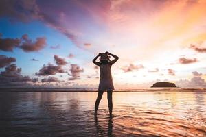 vue arrière d'une femme de voyage adulte se détendre sur le sable de la plage avec ciel coucher de soleil crépusculaire