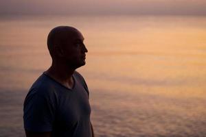 silhouette masculine sur fond de mer au coucher du soleil ressemble à côté seul. homme appréciant photo