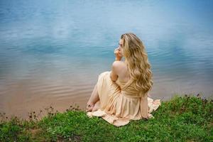 belle fille triste assise sur la rive du lac dans une robe, le concept de solitude photo