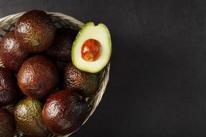 avocats mûrs dans un panier sur un tableau noir, avec un fruit coupé et une pierre. photo