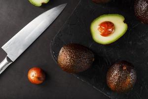 avocats entiers et tranchés avec un couteau sur une table noire texturée noire, maçonnerie plate. photo