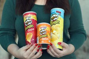 la jeune fille détient quelques packs de cylindres de croustilles pringles. pringles est une marque de croustilles de pommes de terre appartenant à la société kellogg photo