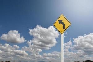 panneau de signalisation, signe de courbe de flèche gauche sur poteau blanc près de la route principale avec fond de ciel bleu, mise au point douce et sélective. photo