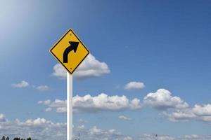 panneau de signalisation, signe de courbe de flèche gauche sur poteau blanc près de la route principale avec fond de ciel bleu, mise au point douce et sélective.