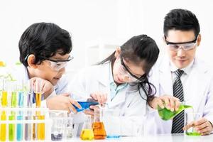 de jeunes enfants asiatiques portant une robe de scientifique blanche et faisant un tube à essai chimique pendant leurs études, apprenant en classe de sciences avec un enseignant. concept d'éducation des jeunes enfants par expérience, plaisir et plaisir en classe photo