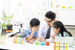 un jeune garçon et une fille asiatique sourient et s'amusent tout en apprenant une expérience scientifique en laboratoire avec un enseignant en classe. étudier avec du matériel scientifique et des tubes. notion d'éducation. photo