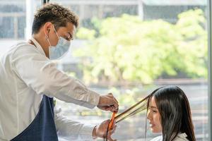 mise au point sélective sur le visage de femmes asiatiques avec des cheveux élégants tout en coupant les cheveux et en portant un masque chirurgical tout en coiffant les cheveux pour le client. occupation professionnelle, service de beauté et de mode nouvelle normalité photo