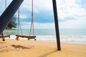 mise au point sélective à la balançoire en bois sur le sable à la plage. avec vue sur les vagues et la mer avec nuage, ciel bleu. vacances d'été sur une belle île tropicale. destination touristique. photo