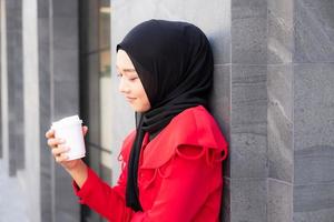 belles femmes islamiques d'asie de l'est portant le hijab avec une robe formelle. tenant une tasse de café et marchant dans la zone urbaine, se sentant heureux et souriant. concept de style de vie des gens avec espace de copie. photo