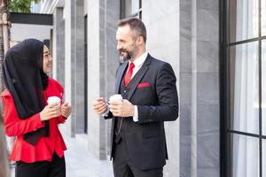 mise au point sélective sur le visage des hommes. photo en plein air d'un homme et d'une femme d'affaires intelligents en costume formel tenant une tasse de café tout en se tenant dans le quartier central des affaires. environnement de travail diversifié.