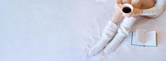 moment de paresse au lit. jeune femme en chaussettes tricotées sur une feuille blanche lisant photo
