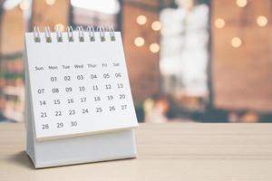 calendrier de bureau en papier blanc sur table en bois avec rendez-vous d'arrière-plan bokeh flou et concept de réunion d'affaires photo