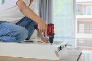 homme assemblant des meubles de table blancs à la maison à l'aide d'un tournevis sans fil photo