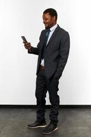 Un homme noir afro-américain souriant en costume d'affaires regarde dans un fond de mur blanc de smartphone photo