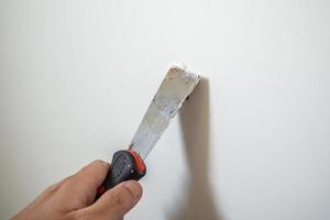 homme réparant un mur blanc fissuré avec une spatule photo