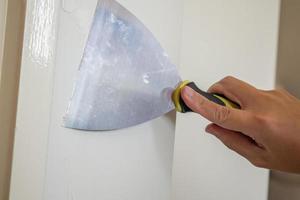 homme réparant un mur blanc fissuré avec une spatule photo