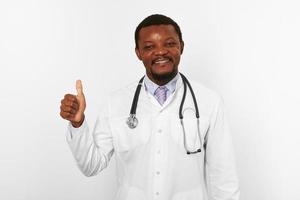 homme médecin barbu noir souriant en robe blanche avec stéthoscope montre comme un geste, fond blanc photo