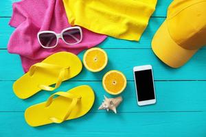 accessoires d'été sur fond en bois bleu. tongs jaunes, serviettes, lunettes de soleil, casquette, téléphone portable et oranges. maquette et vue de dessus photo